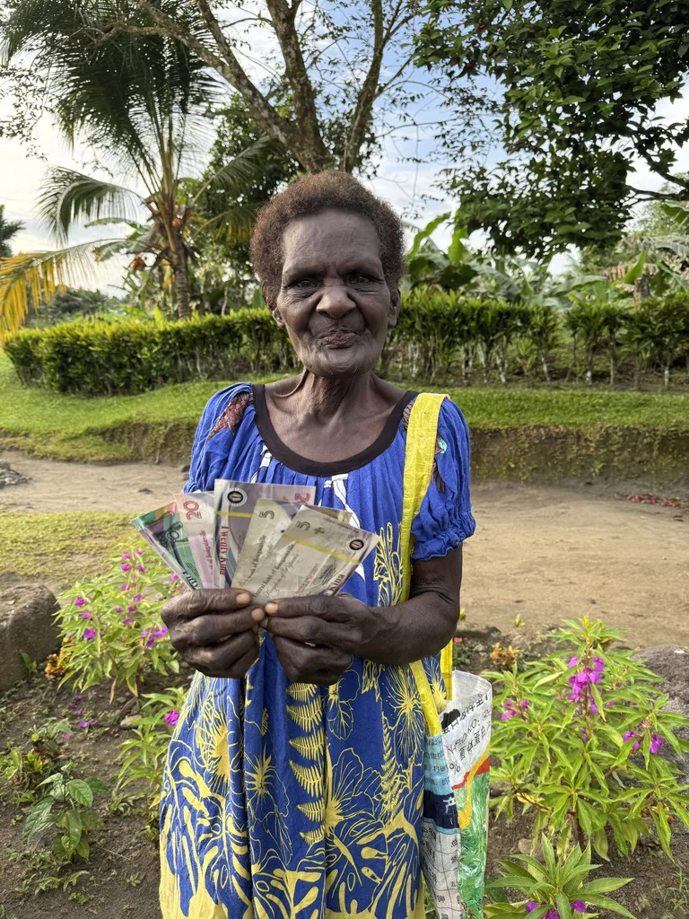 ブーゲンビル島内にあるマイクロネーション「Papaala と Me’ekamui の双王国」のお金を広げて見せるおばさん