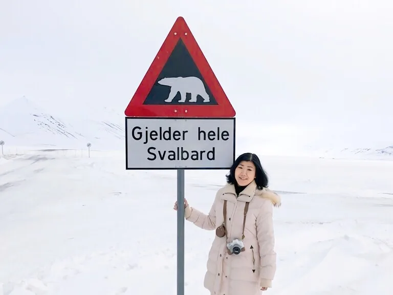 北極圏ロングイェールビーン(Longyearbyen)の雪山とホッキョクグマ生息エリアの看板の前で記念撮影している観光客