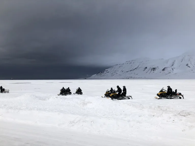 スピッツベルゲン島の雪原を走るスノーモービルのグループ