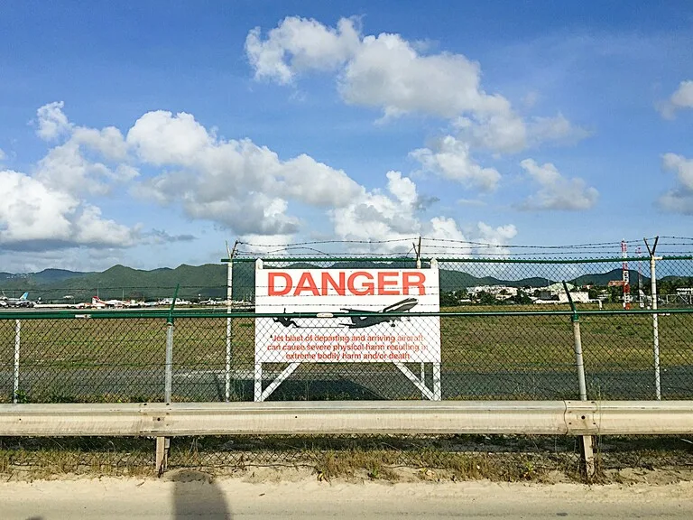 マホビーチと空港の間に立つDangerの警告看板