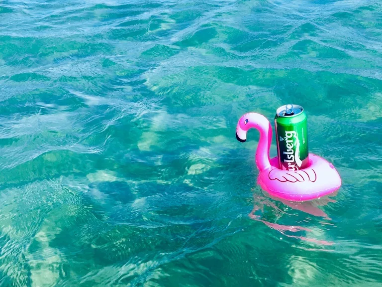 海に浮かぶフラミンゴの浮き輪に載ったビール